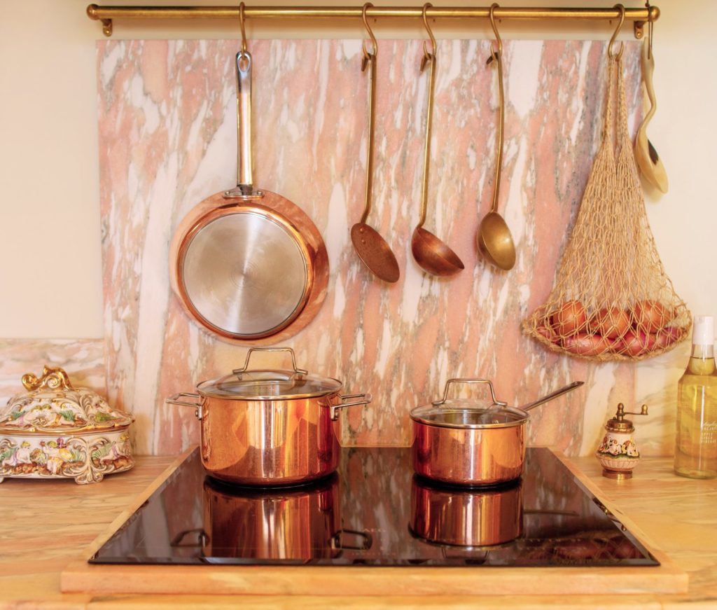 Reclaimed pink Norwegian Rose marble splash back and worktop with copper vintage utensils and copper pans